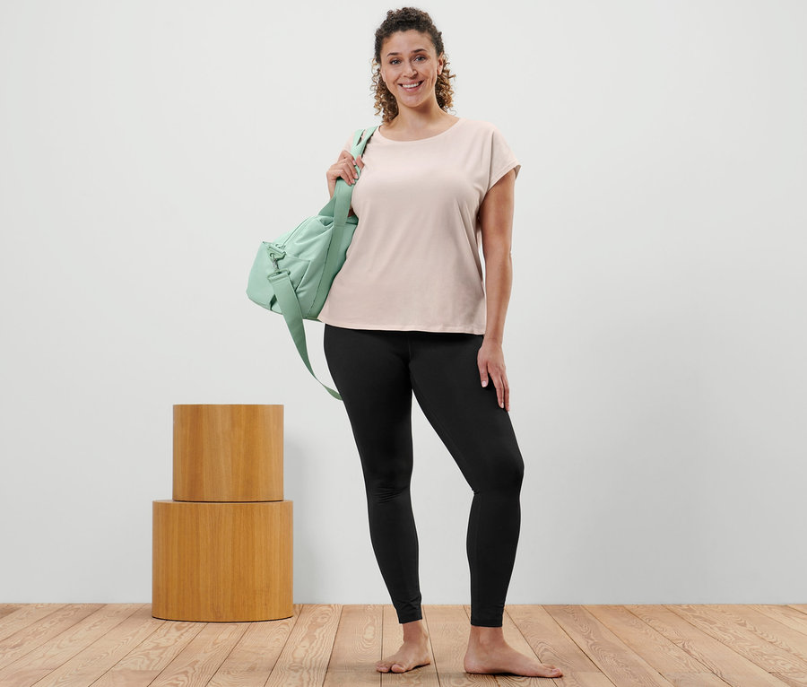 Femme posant en T-shirt de sport blanc cassé, legging de sport et sac de sport vert sur l'épaule.