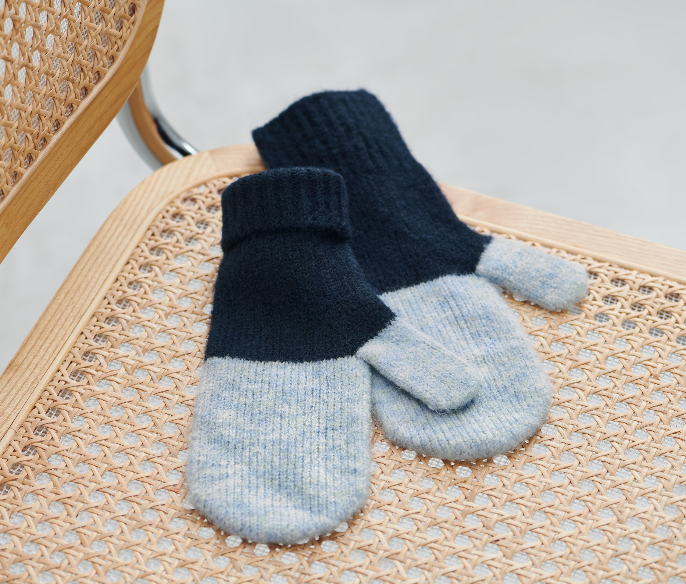 Des moufles en maille bleu foncé sont posées sur une chaise en osier.