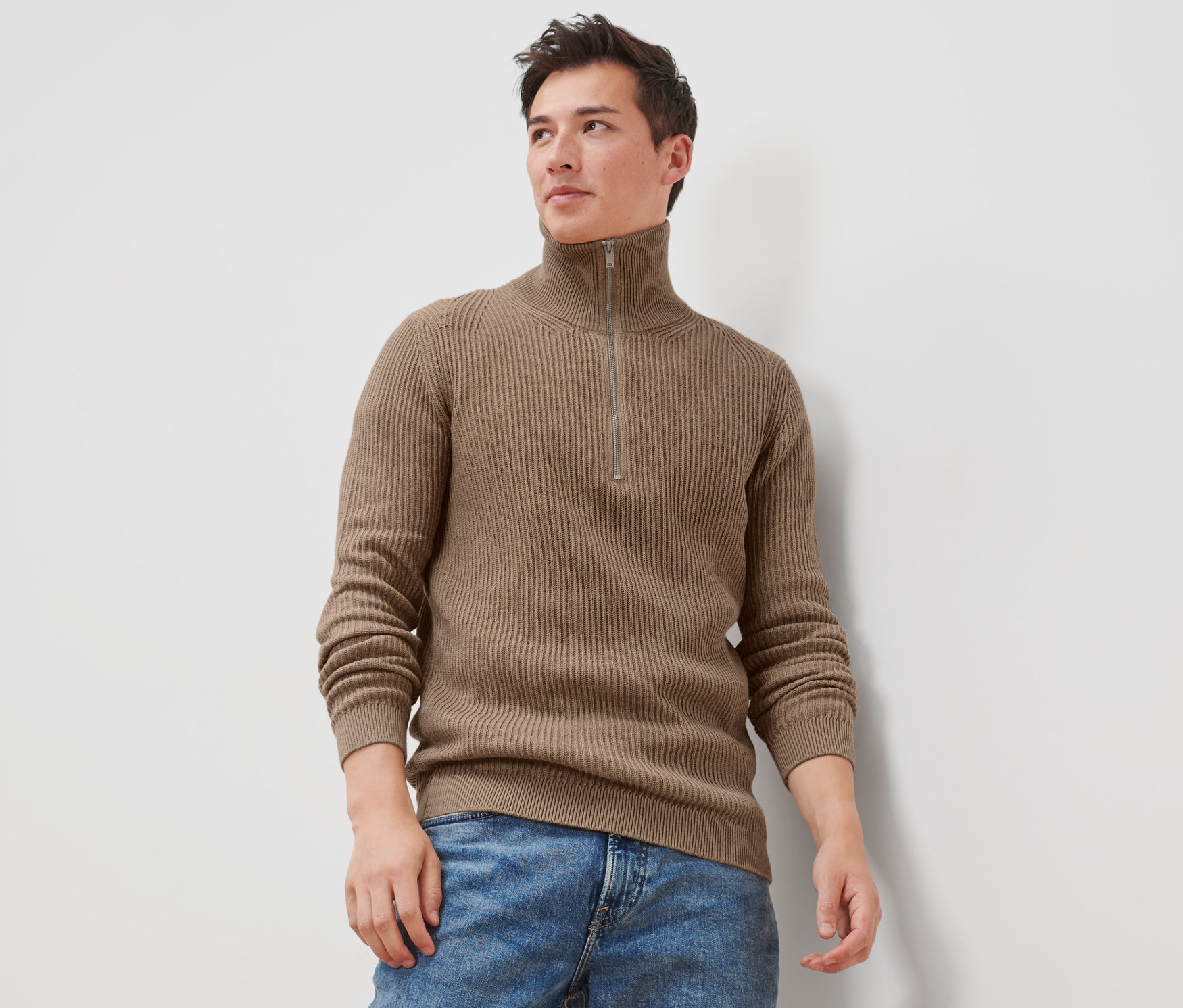 Un homme porte un pull camionneur et un jean.