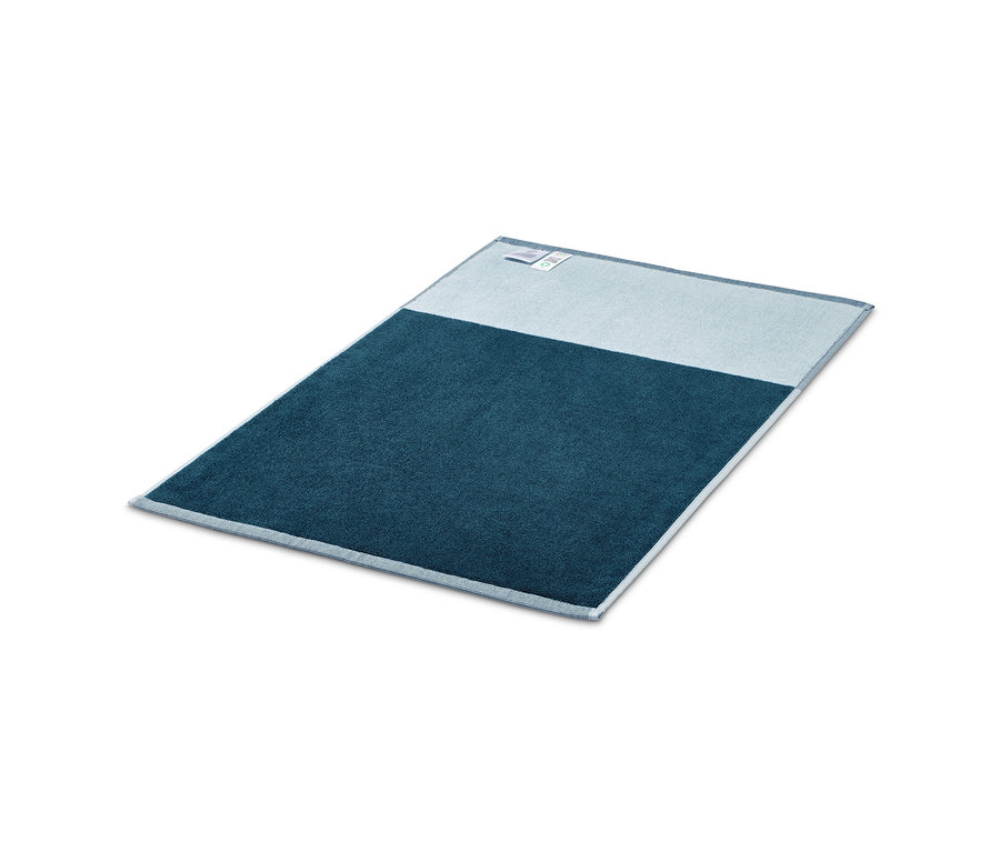 Un tapis de douche jacquard bleu posé sur un fond blanc.