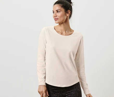 Femme posant dans un t-shirt de sport à manches longues blanc cassé et tenant une bouteille d'eau.