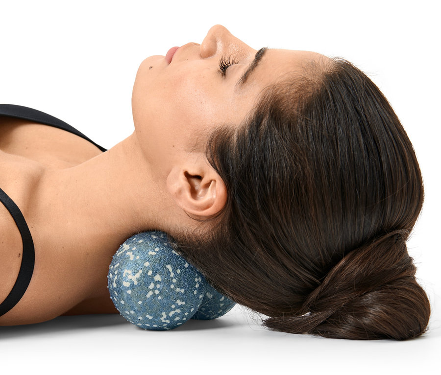 Une femme est allongée sur le dos avec une double balle de massage sous son cou.