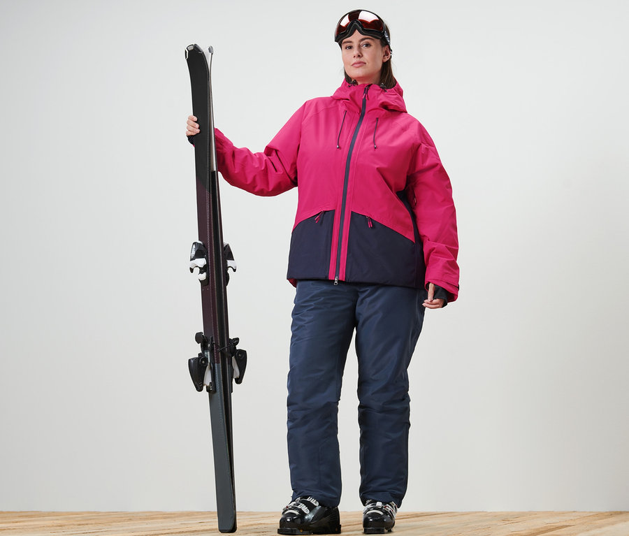 Femme tenant des skis, portant une veste de ski et un pantalon de ski.