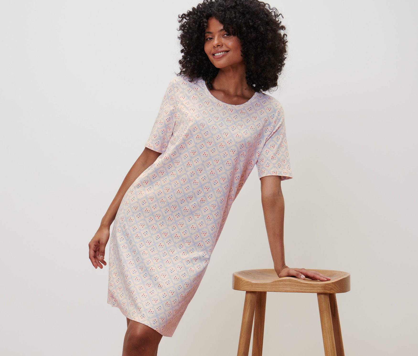 Femme posant en chemise de nuit à manches courtes, appuyée sur un tabouret en bois.