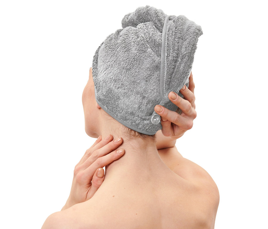 Une femme fixe une serviette turban grise sur sa tête.