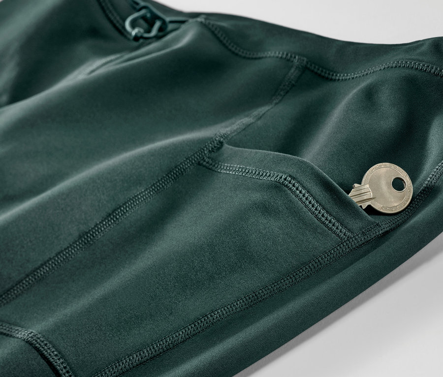 Détail d'un legging thermique de course vert foncé avec une clé dans la poche.