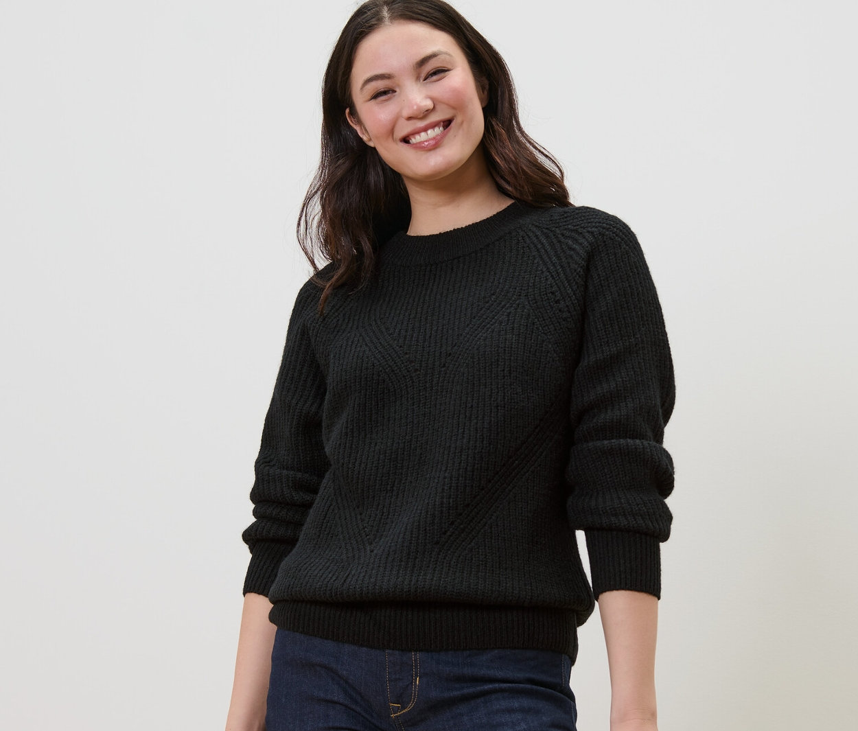 Femme souriante portant un pull en maille noir.