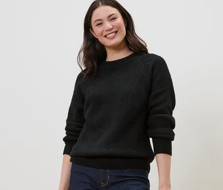 Femme souriante portant un pull en maille noir.