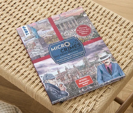 Le livre « Micro Crimes – das Krimi-Suchbuch » est posé sur un tabouret en osier.