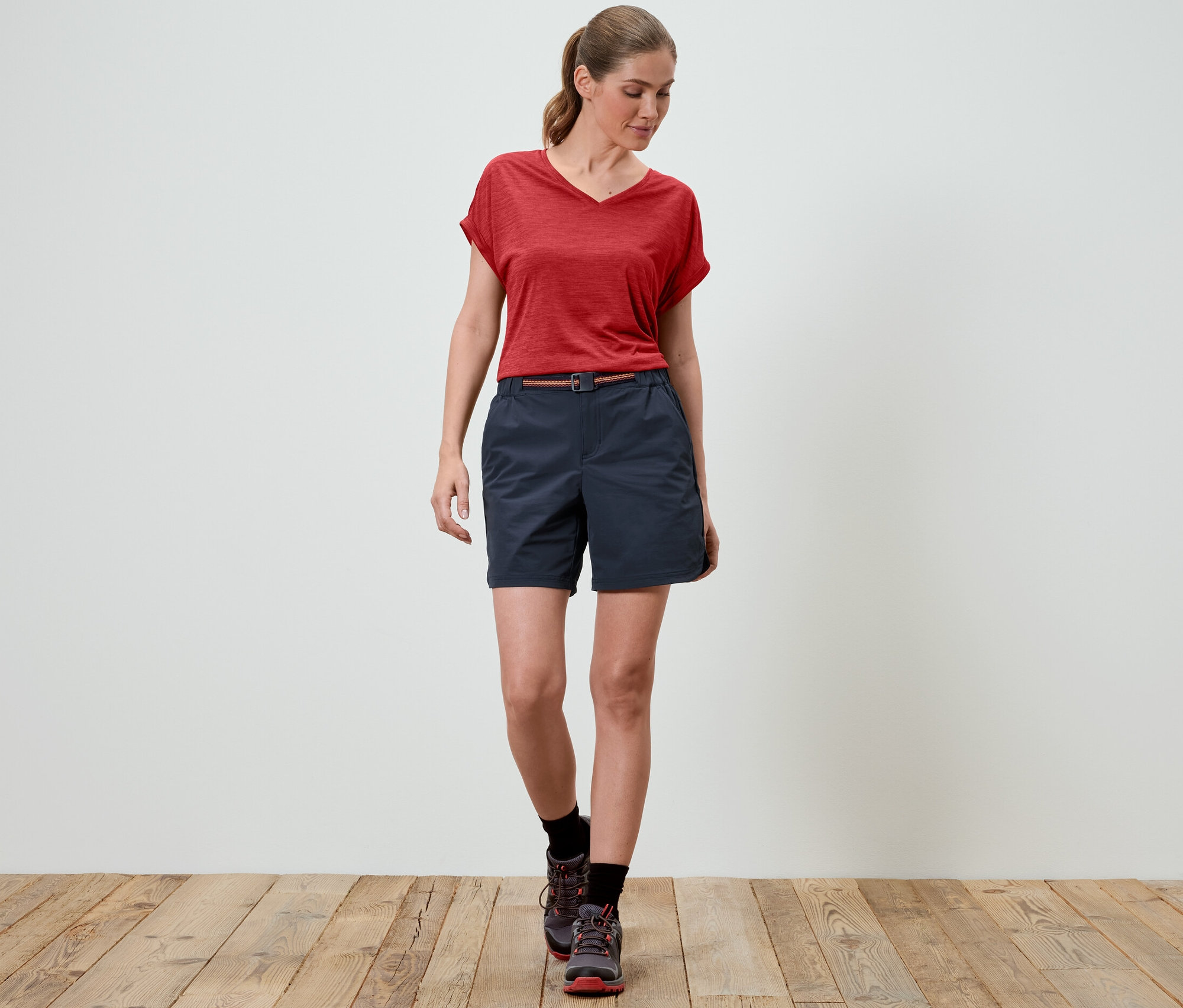 Une femme marche et porte un short de randonnée fonctionnel et un t-shirt rouge.