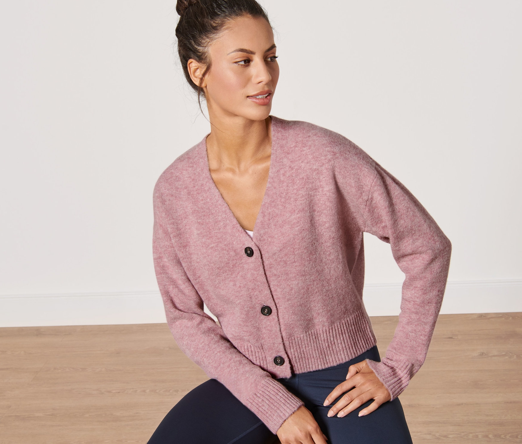 Femme assise sur un tabouret portant un cardigan rose en grosse maille.