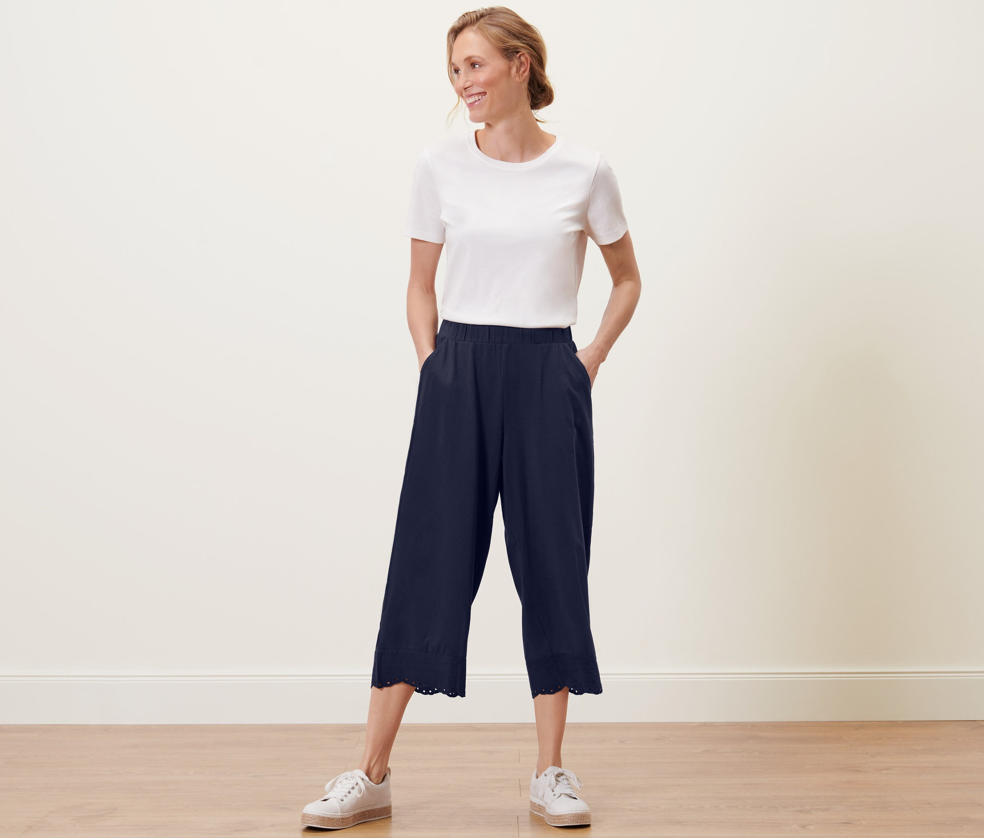 Une femme pose, portant une jupe-culotte à broderie marine et un t-shirt blanc.