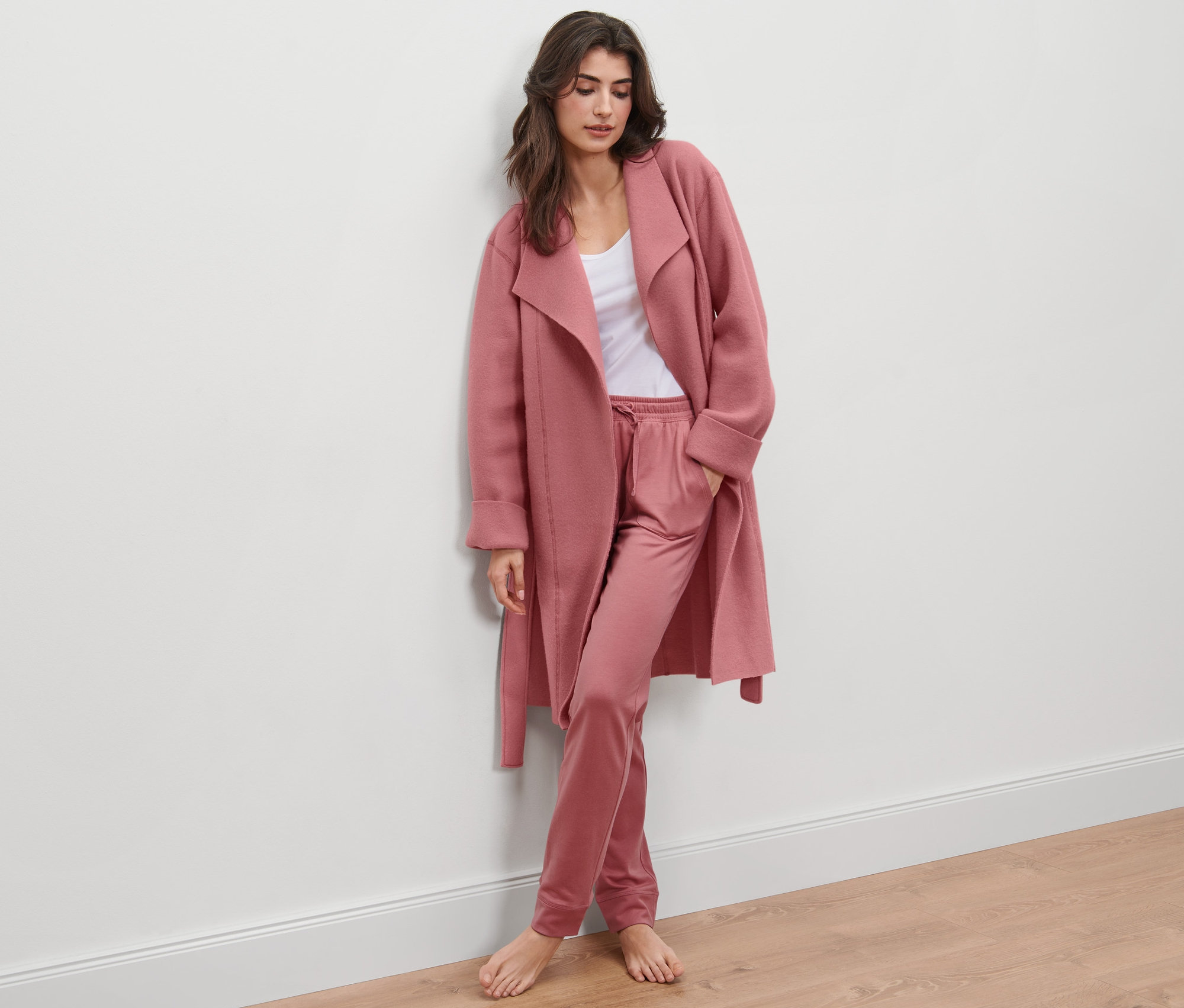 Femme appuyée contre un mur portant un peignoir en polaire et un pantalon.