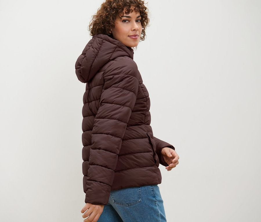 Femme posant dans une veste matelassée à capuche marron foncé.
