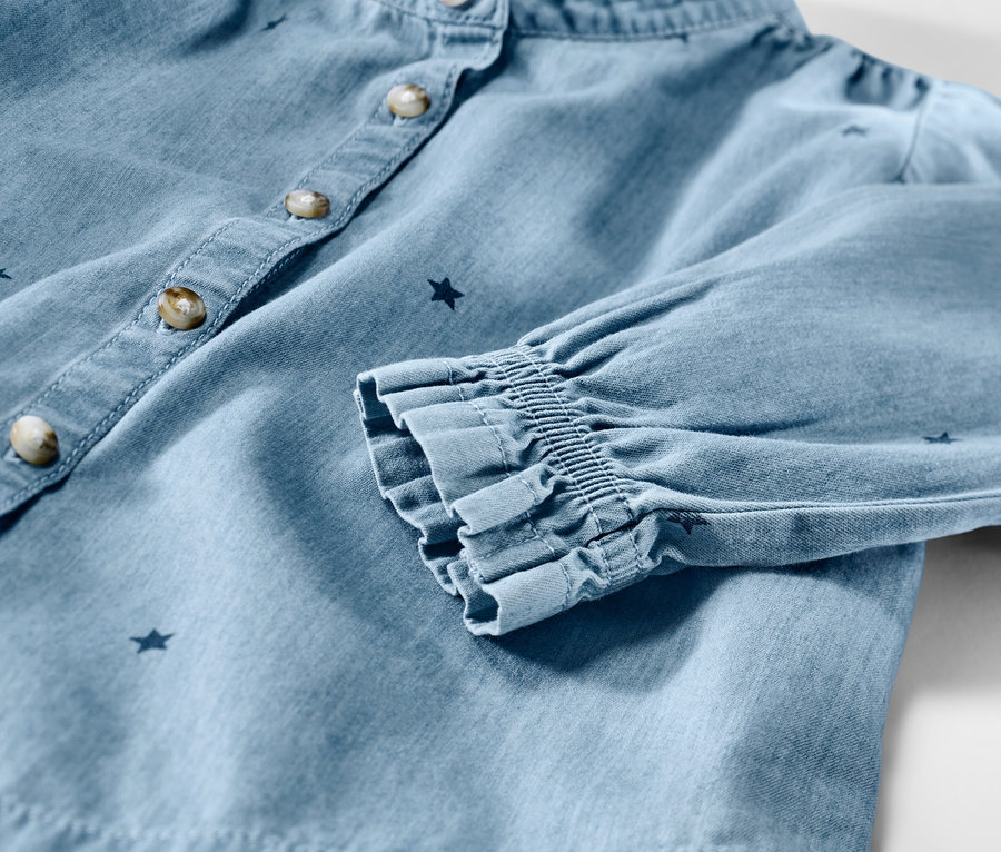 Gros plan sur une chemise en chambray pour enfant avec des étoiles, des boutons et des manches froncées.