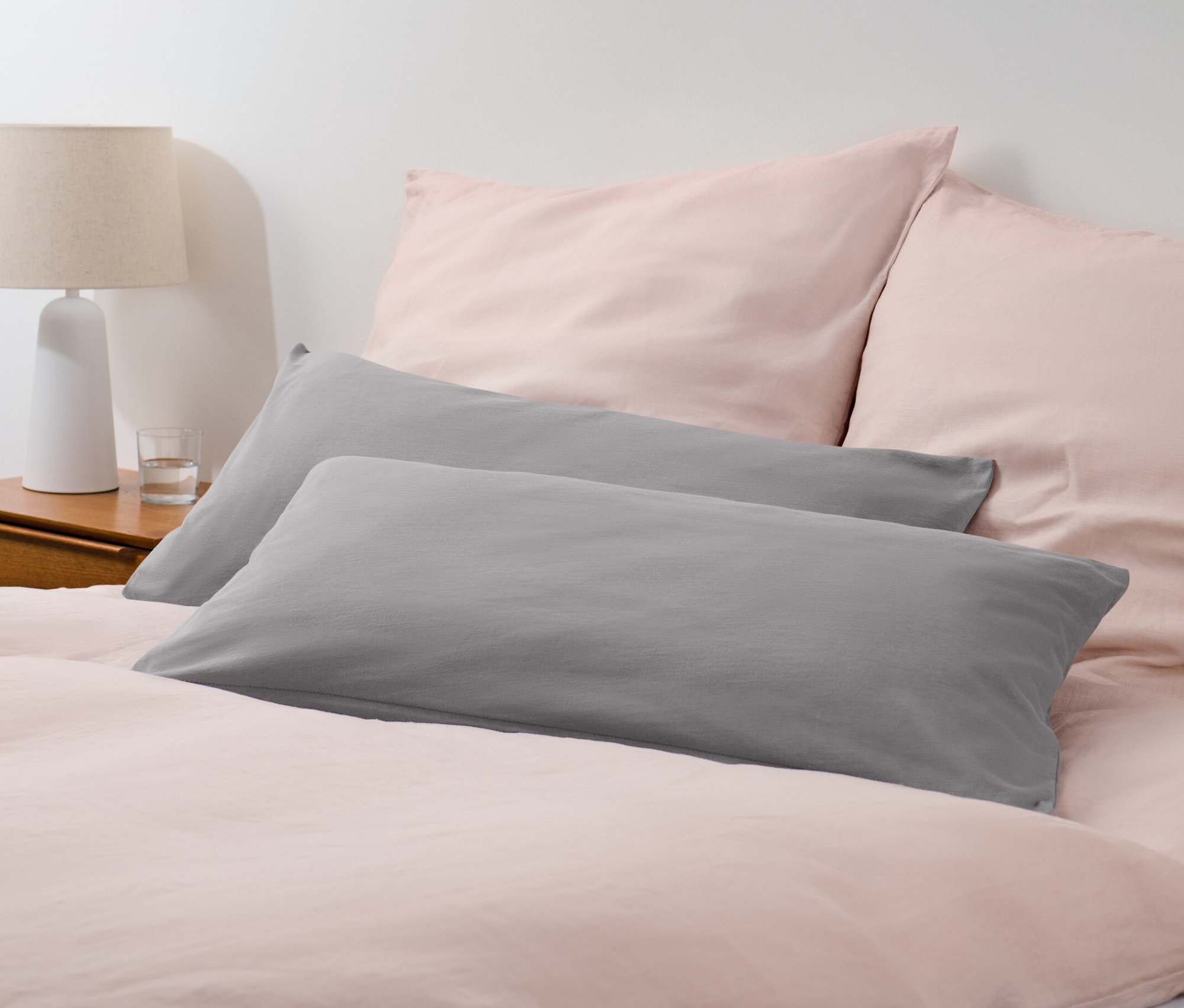Deux taies d'oreiller en jersey gris sur un lit avec du linge de lit rose.