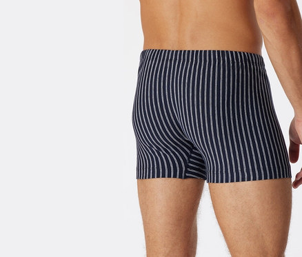 Un homme vu de dos porte un short SCHIESSER en coton bio bleu foncé avec des rayures blanches.