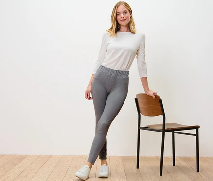 Une femme pose en legging gris aspect jean à côté d'une chaise.