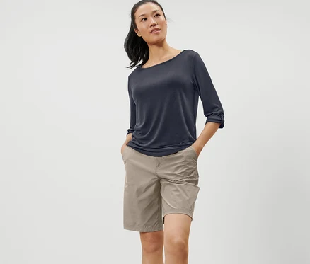 Femme debout, les mains dans les poches, portant un t-shirt fonctionnel bleu à manches 3/4.