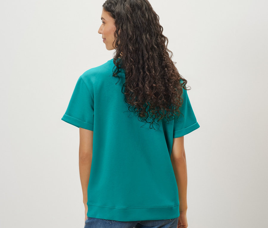 Une femme avec de longs cheveux ondulés porte un t-shirt en mélange avec modal turquoise et un jean.