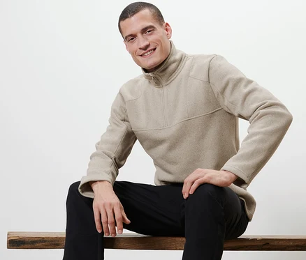 Un homme est assis sur un banc et porte un pull troyer en tricot polaire.