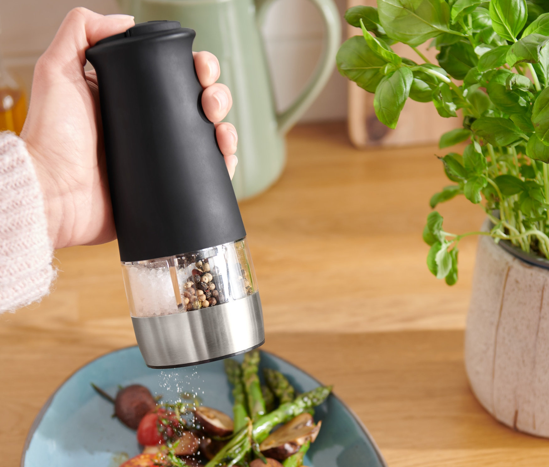 Une personne assaisonne une assiette de légumes avec un moulin à sel et à poivre 2 en 1 électrique.