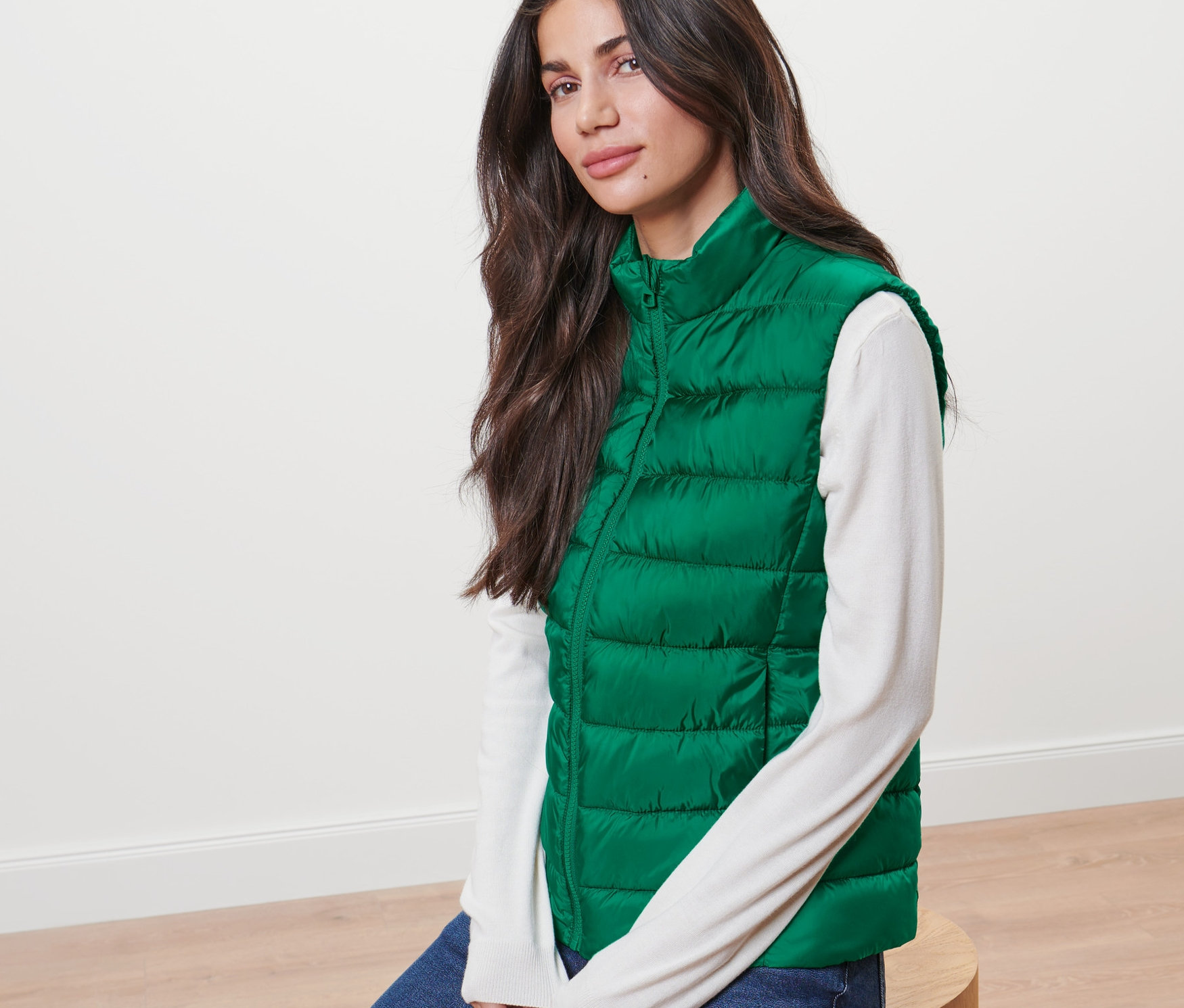 Femme assise portant une veste sans manches matelassée verte.