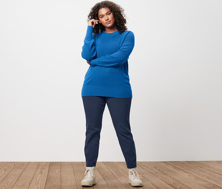 Femme posant en pull en maille fine, pantalon stretch bleu foncé et chaussures de sport doublées en cuir.