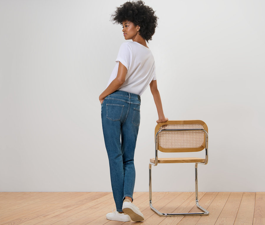Femme posant en jean slim – Coupe « Emma » bleu moyen et t-shirt blanc à côté d'une chaise.