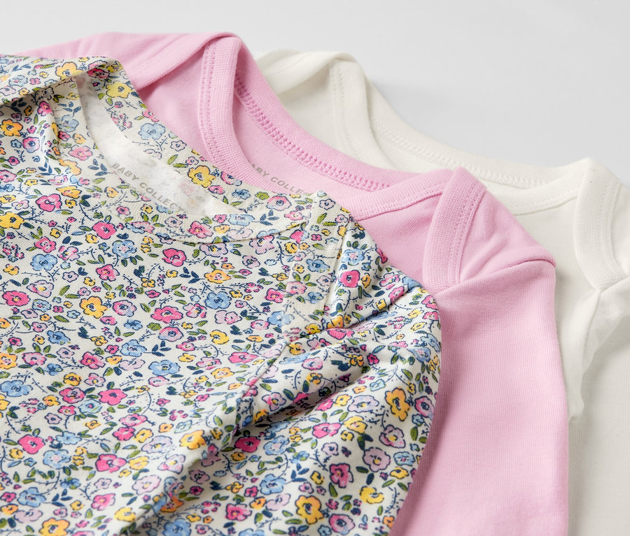 Trois bodys roses pour bébé avec fonction évolutive sont posés les uns sur les autres.
