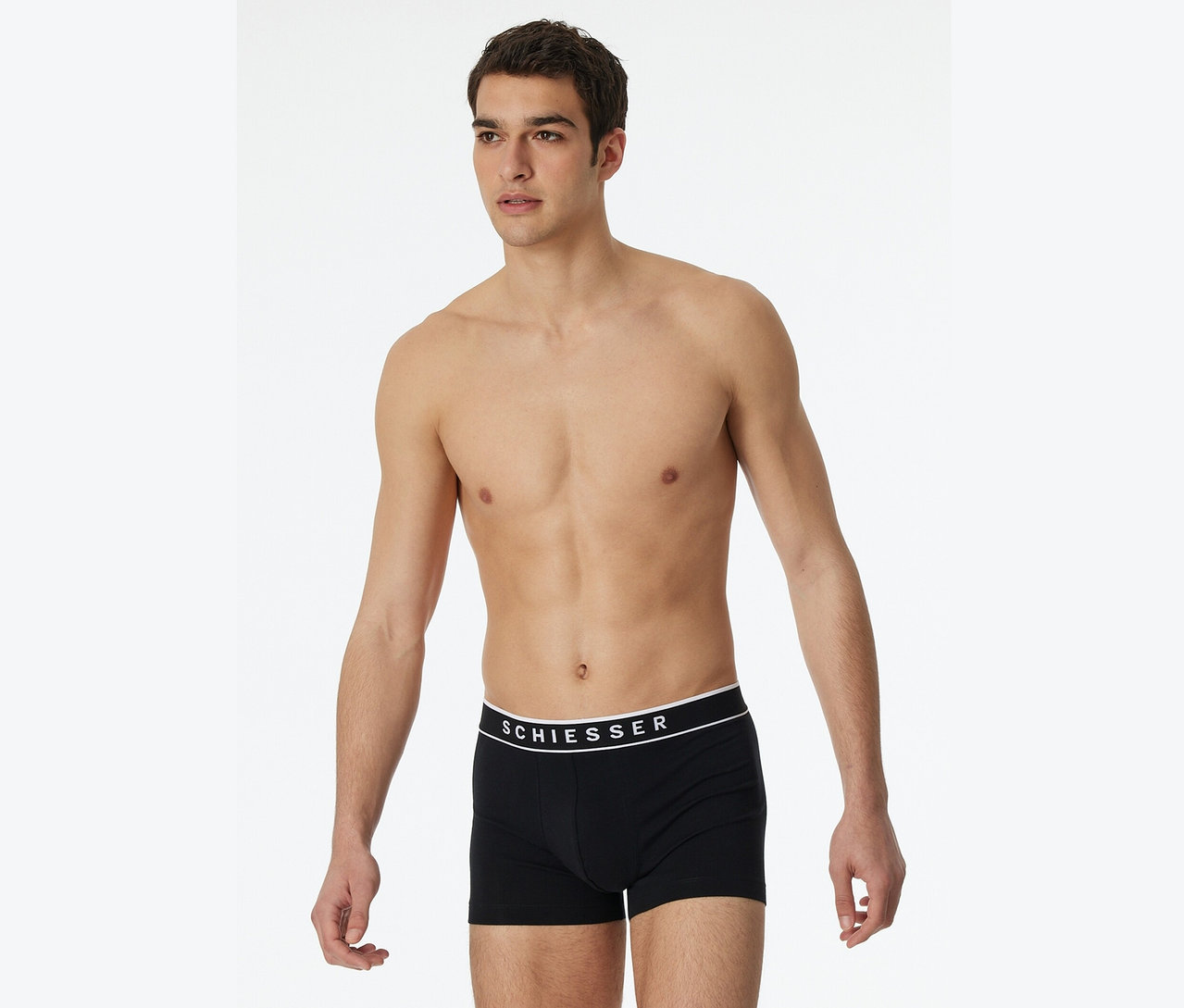 Un homme pose torse nu en boxeur Schiesser noir.