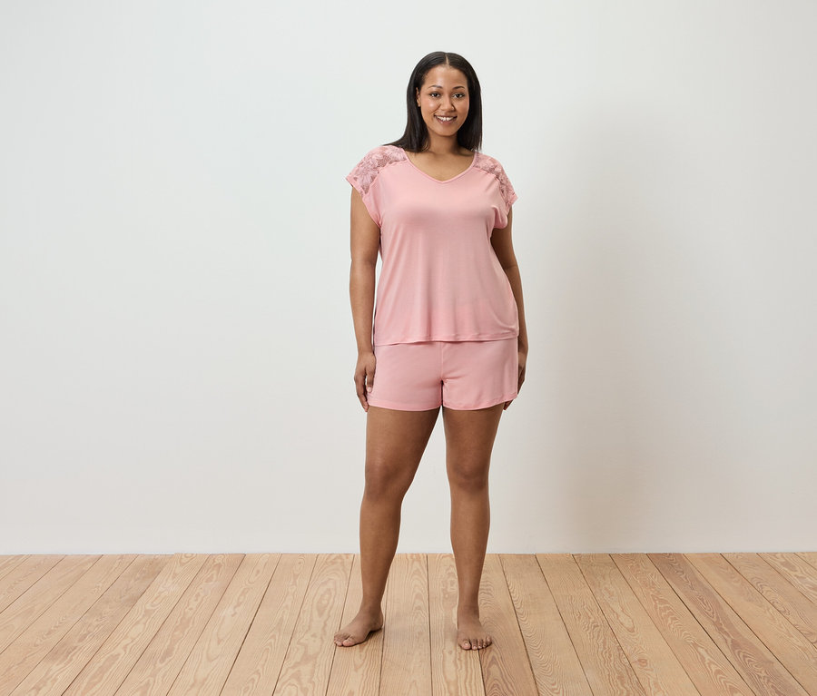 Une femme debout porte un pyjama rose avec de la dentelle aux épaules.