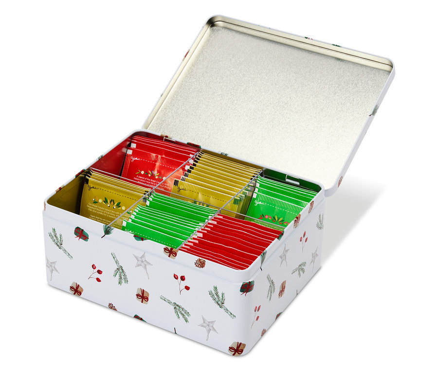 Boîte métallique blanche ouverte à motif de Noël remplie de sachets de thé rouges, verts et jaunes.