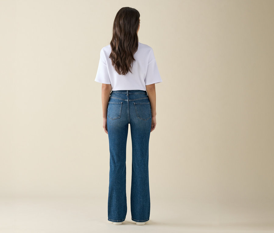 Une femme aux longs cheveux bruns se tient dos à l'appareil photo, portant un t-shirt blanc et un jean bleu.
