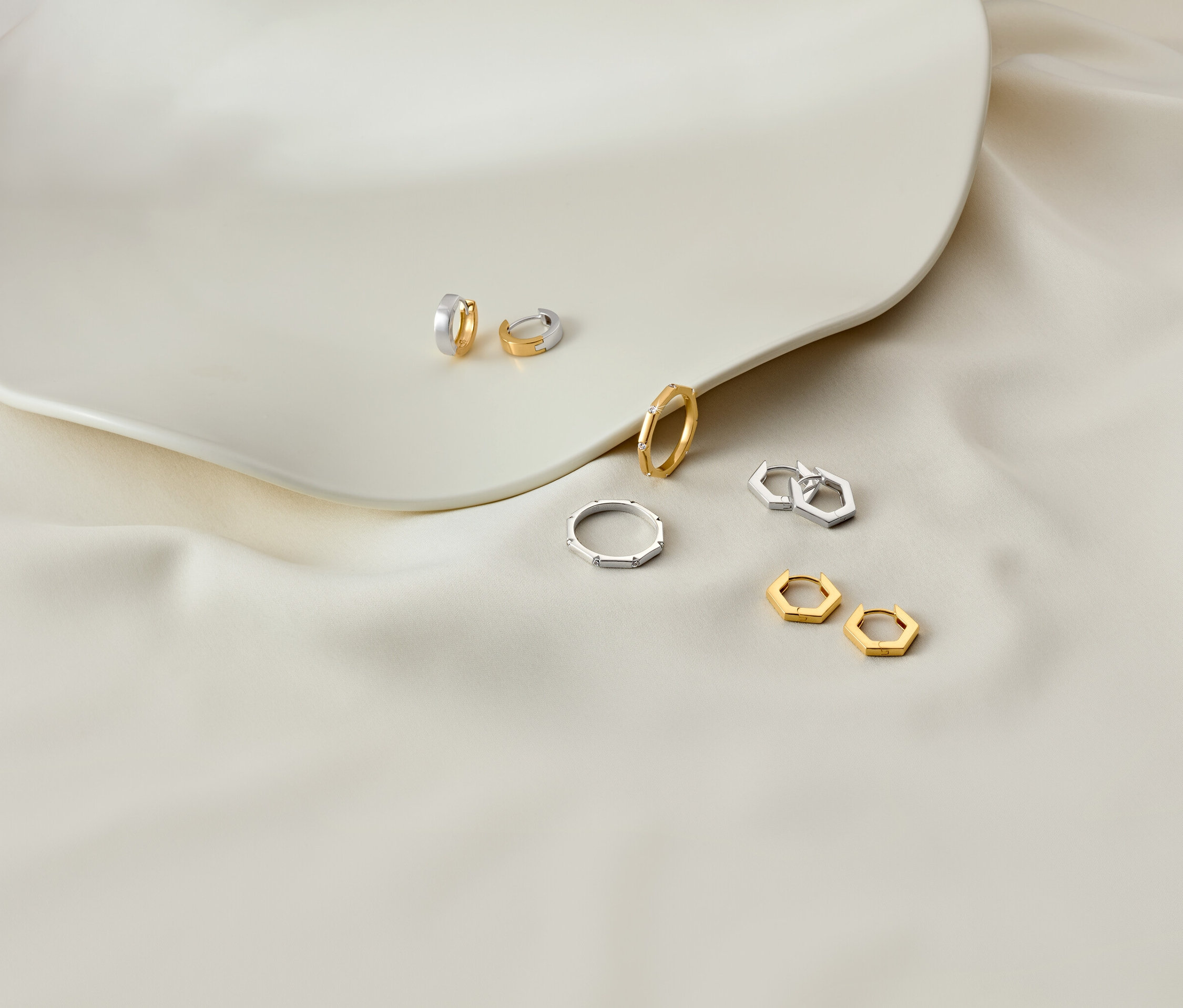 Boucles d'oreilles et bagues sur une assiette blanche et un tissu blanc.