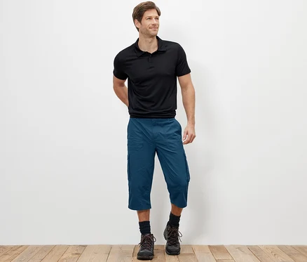 Un homme debout portant un bermuda cargo bleu longueur 3/4.