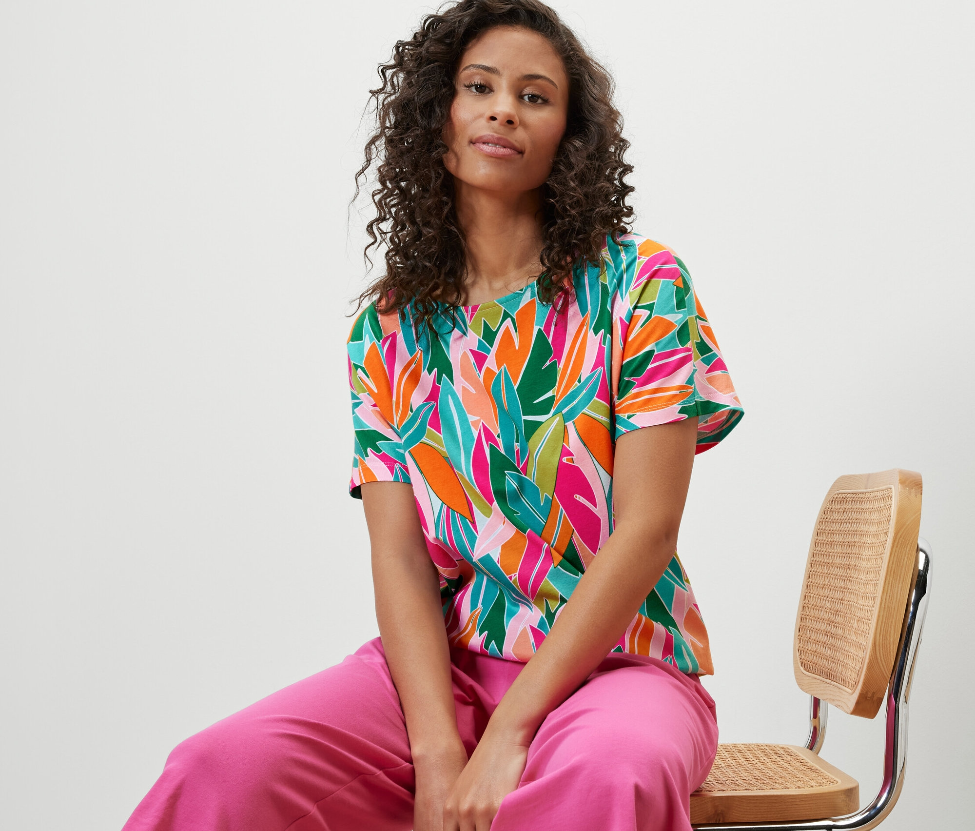 Femme assise sur une chaise portant un chemisier à encolure dégagée avec un imprimé intégral.