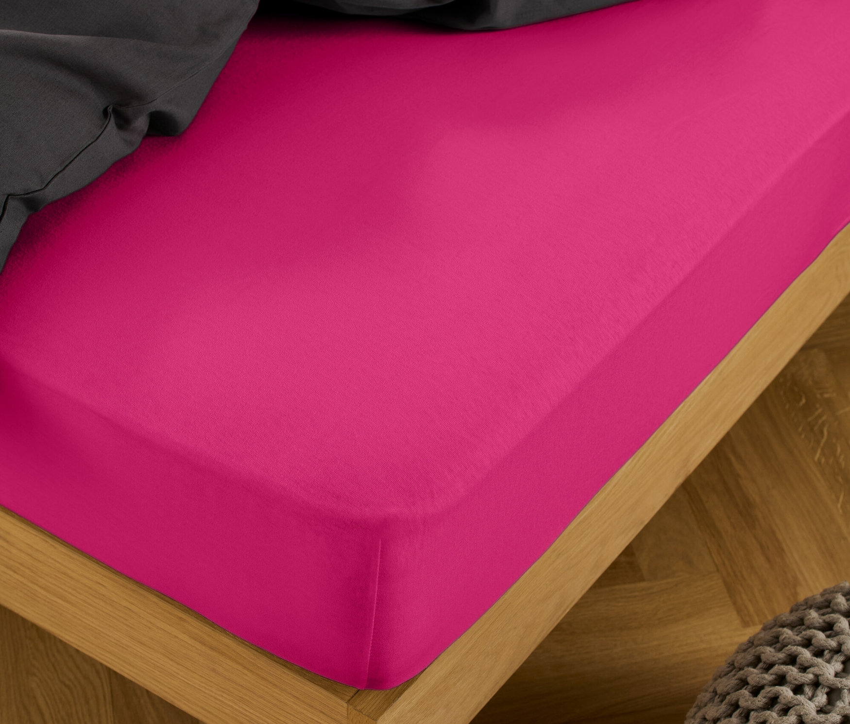Un drap-housse en jersey rose vif de taille standard et double sur un lit avec une couverture grise.