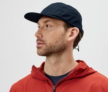 Un homme portant une veste orange et une casquette pliable regarde vers la gauche.