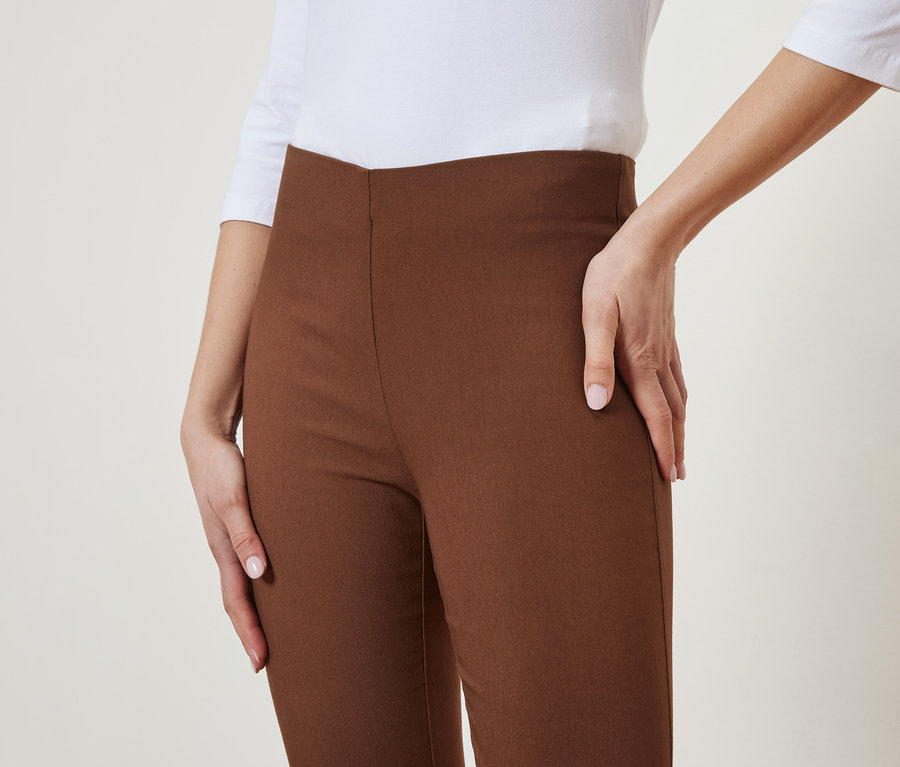 Une femme pose en pantalon marron et haut blanc.