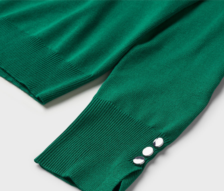 Gros plan sur un pull vert à manches longues avec des boutons décoratifs aux poignets.