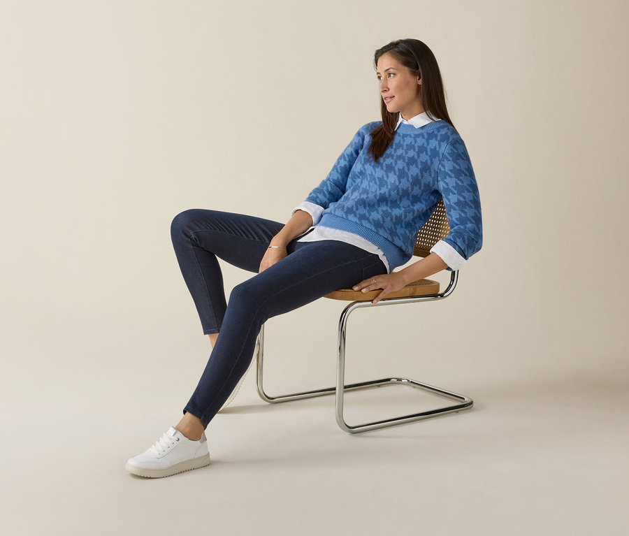 Une femme est assise sur une chaise et porte un pull bleu et des baskets blanches Tom Tailor en PU.