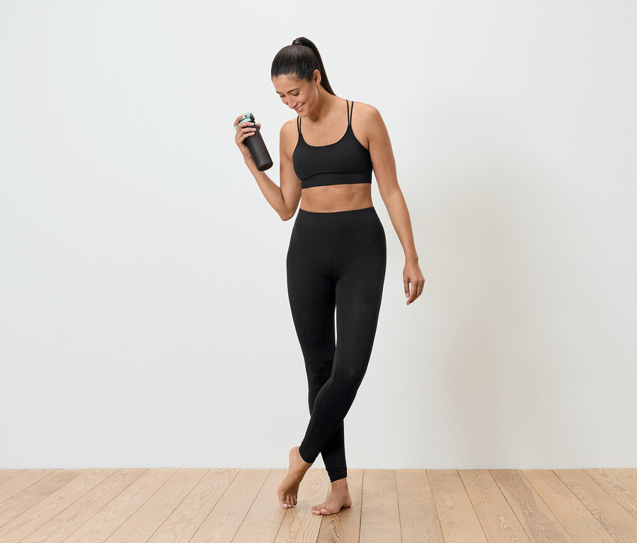 Femme en tenue de sport noire tenant une bouteille d'eau.