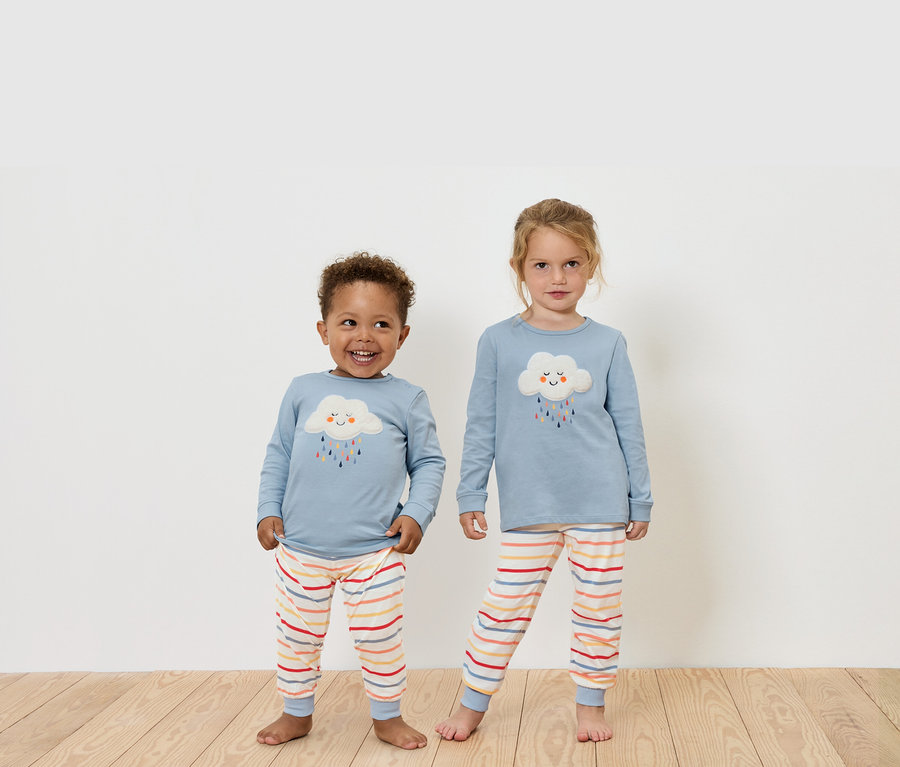 Deux enfants debout sur un plancher en bois portent des hauts bleus à manches longues et des pantalons rayés.