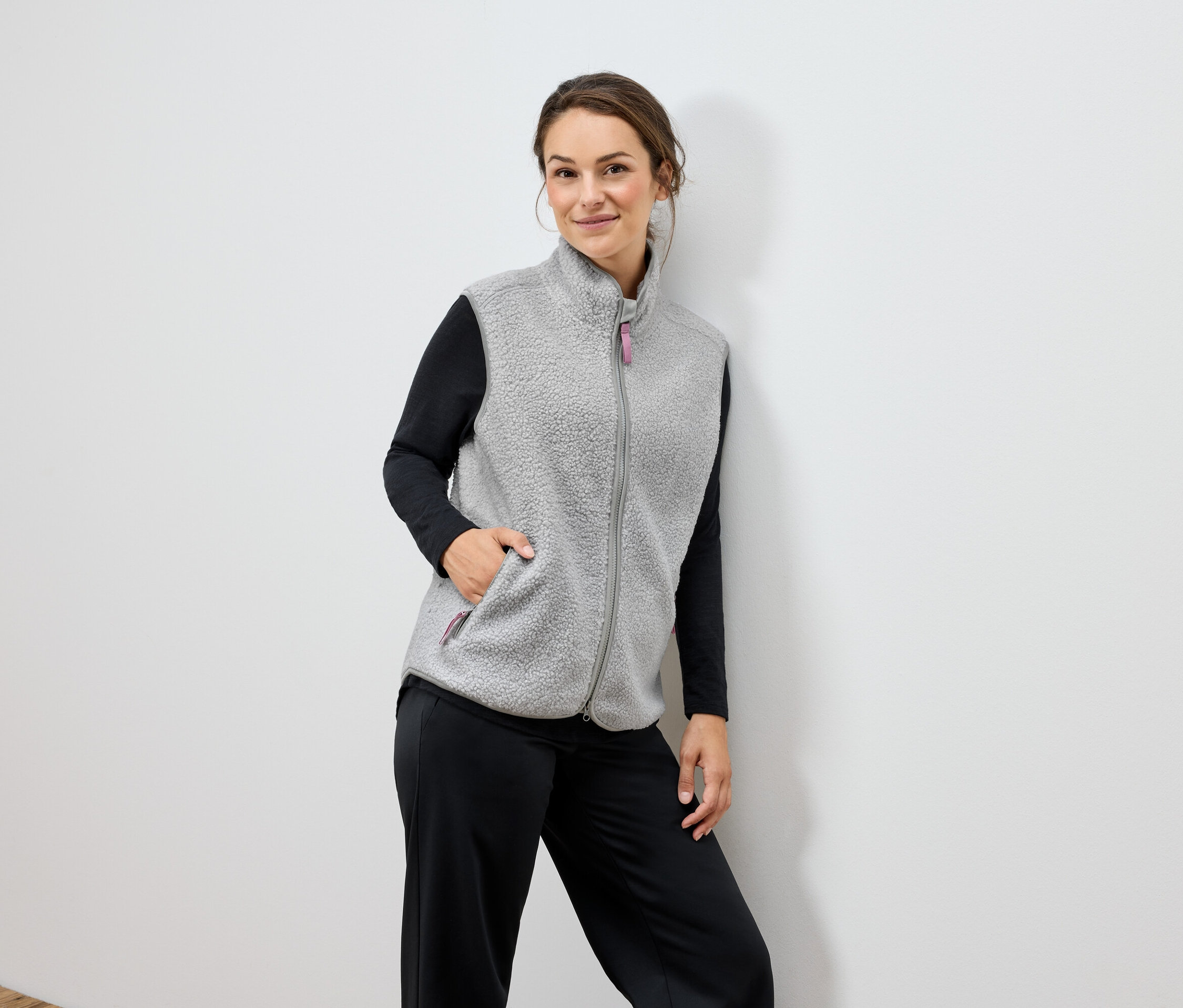 Une femme porte une veste en polaire grise et un pantalon noir.