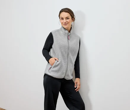 Une femme porte une veste en polaire grise et un pantalon noir.