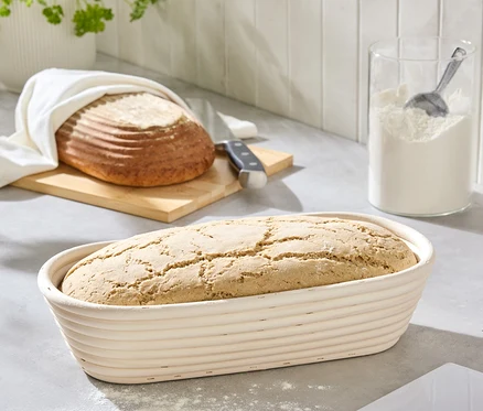 Pain dans un banneton sur le comptoir à côté de la farine et du pain sur une planche à découper.