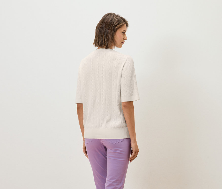 Une femme, dos à la caméra, porte un haut tricoté crème à manches courtes et un pantalon violet.