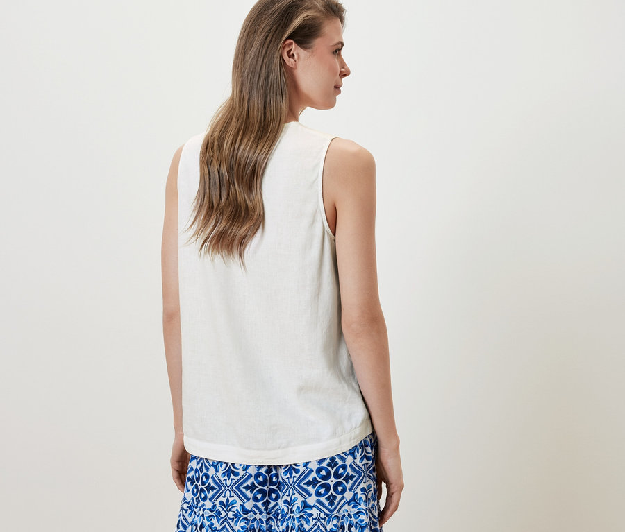 Une femme porte un chemisier sans manches en lin blanc et une jupe bleue.