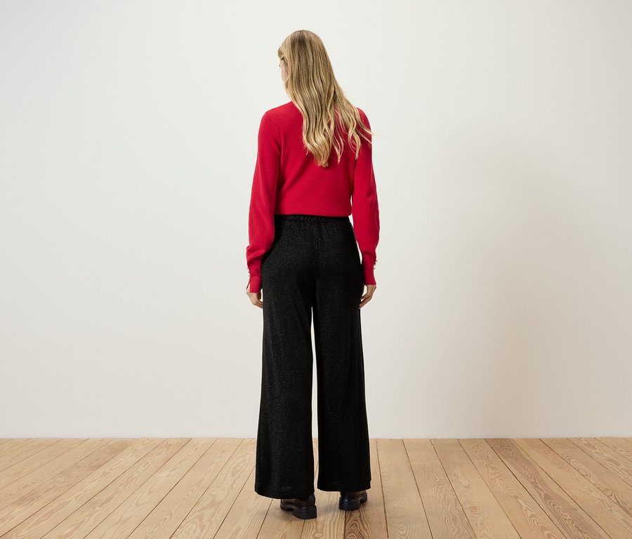 Vue arrière d'une femme blonde portant un pull rouge et un pantalon noir.